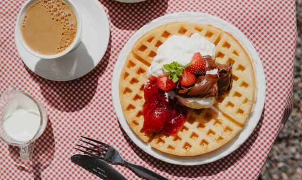 En våffla med grädde och nutella och en kopp kaffe på en rutig duk.