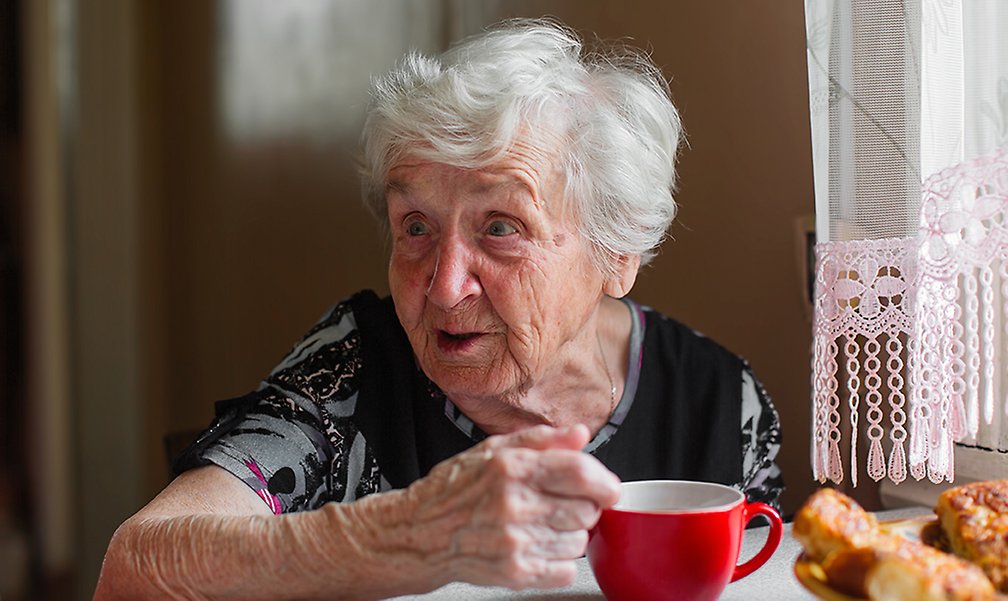 Äldre dam med en kaffekopp framför sig.