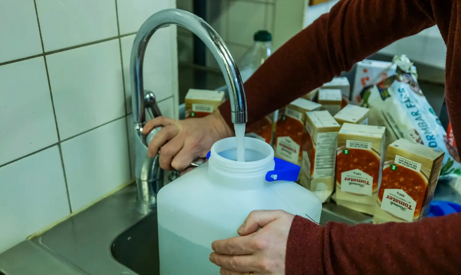 Person som tappar upp vatten i en plastdunk. Konserver står på diskbänken. Foto: MSB